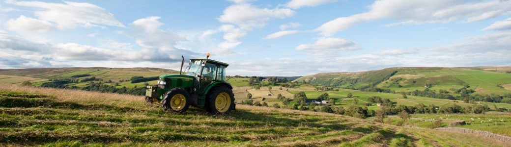 A green tractor mowing a hay meadow with a traditional Nidderdale landscape behind